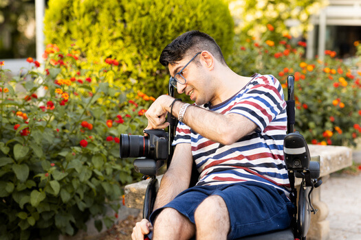 A white man with dark hair in a wheelchair taking photos of red flowers with a camera that has a telescopic lens.